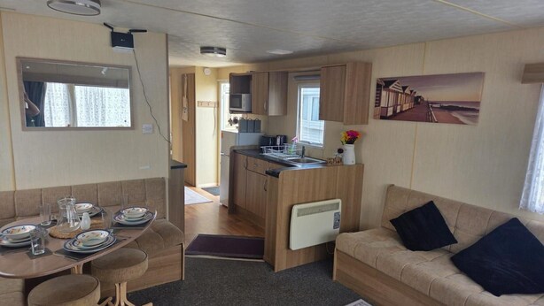 Interior compacto de una caravana, con comedor, cocina americana y sofá.