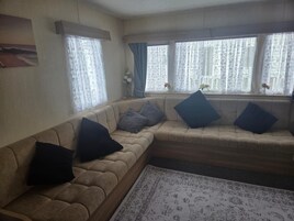 Una sala de estar con un sofá color beige, un tapete estampado y una ventana con cortinas de gasa.