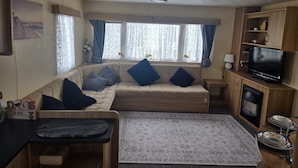 Interior acogedor de una caravana con sofá, una mesita, televisor y zona de cocina.