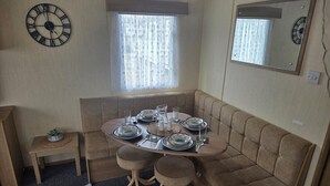 Una habitación compacta con una mesa de comedor preparada para cuatro personas, un sofá, una mesita auxiliar y un reloj en la pared.