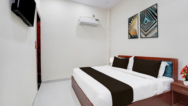 A hotel room with a bed, a TV mounted on the wall, an air conditioning unit, and two abstract wall art pieces. - Classic With Balcony Shri Hari Palace Guest (Mathura)