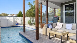 Un espacio exterior cubierto con piscina, mobiliario de mimbre y un ventanal grande.
