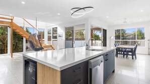 Una cocina moderna con una isla central, un comedor con mesa y sillas, y una escalera que lleva a un espacio exterior.