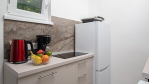 A kitchen with a marble backsplash, a white refrigerator, a black coffee maker, a red kettle, and a bowl of fruit. - Villa with private pool, summer kitchen (Šišan)