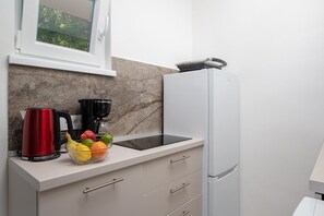 Eine Küche mit Marmorfliesenspiegel, einem weißen Kühlschrank, einer schwarzen Kaffeemaschine, einem roten Wasserkocher und einer Obstschale.