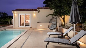 A poolside area with lounge chairs, a hanging chair, and a table with a bottle. - Villa with private pool, summer kitchen (Šišan)