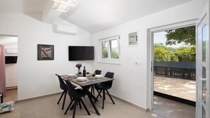 A dining area with a table set for four, a flat-screen TV mounted on the wall, and a sliding glass door leading to an outdoor area. - Villa with private pool, summer kitchen (Šišan)