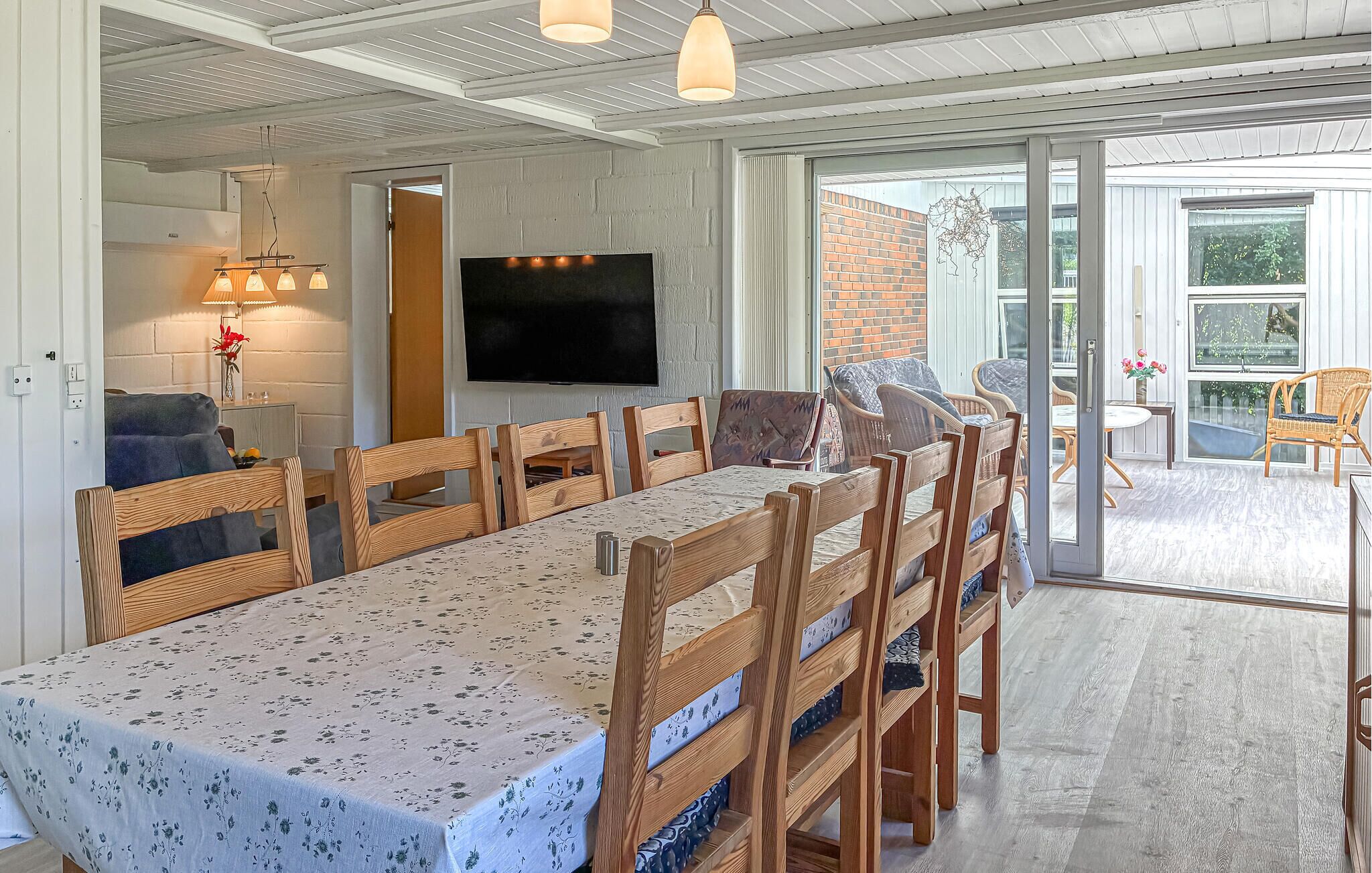 A dining area with a long table, wooden chairs, a TV, and a view of the outside.