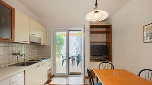 Cocina compacta con lavadora, comedor con mesa y sillas, televisor y puerta corrediza de vidrio que da a un patio exterior.
