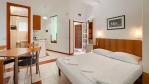 Habitación de hotel con cama, escritorio, silla, kitchenette y puerta que da a otra habitación.
