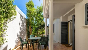 Un patio con una mesa, sillas, un muro blanco y una puerta con contraventanas.