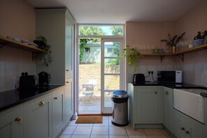 A kitchen with white cabinets, a black countertop, a trash can, and a door leading outside. - Hearth Behind the Shutters - Greenwich (London)