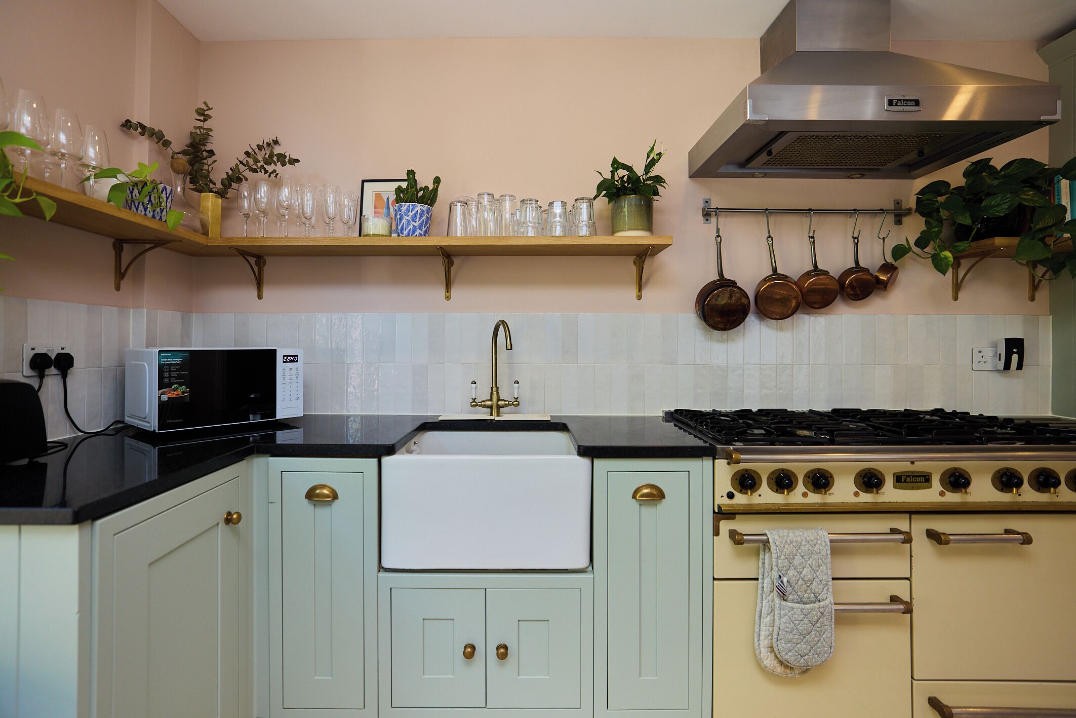 A kitchen with a stove, microwave, and shelves with plants and glassware.