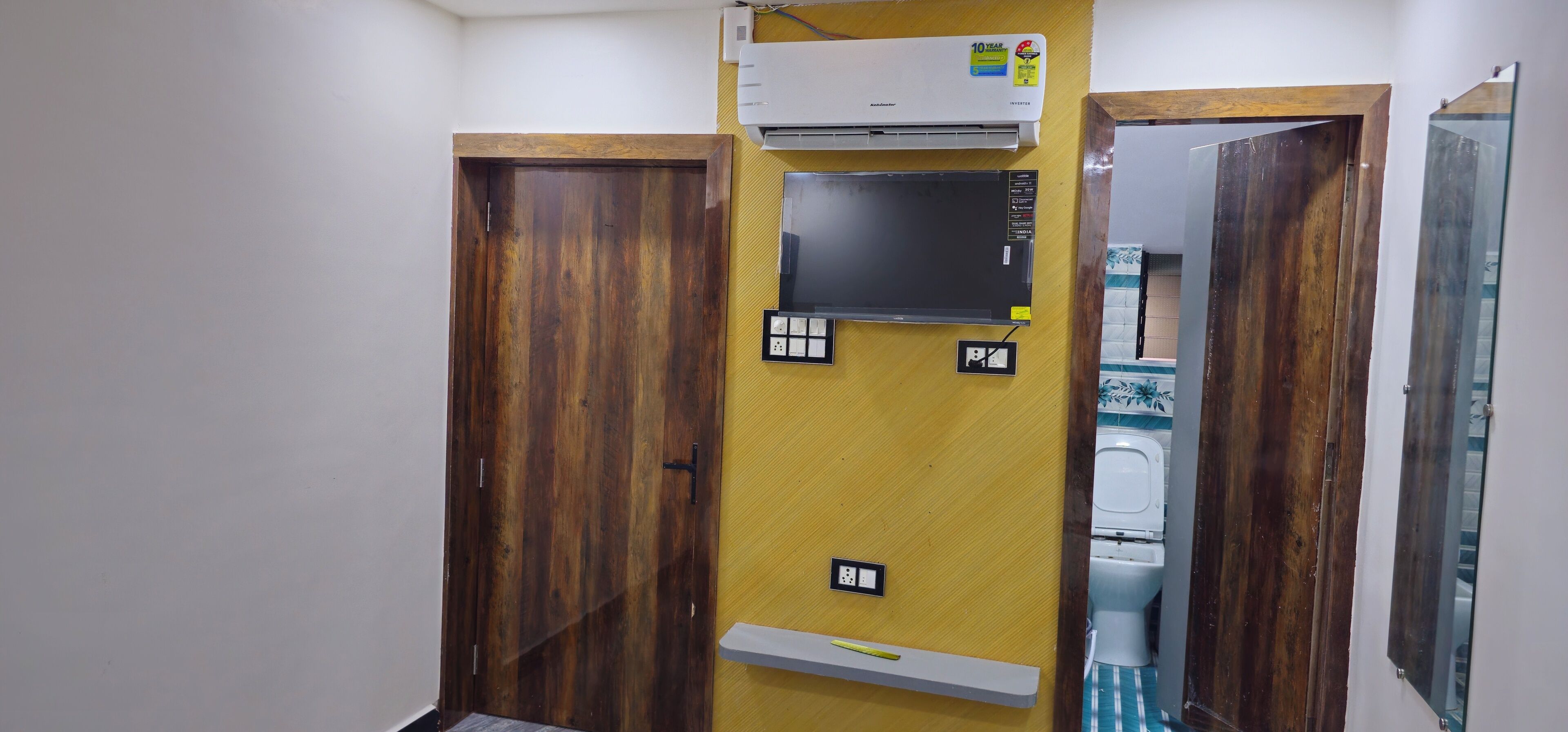 A bathroom with a wooden door, a mirror, a toilet, and an air conditioning unit.