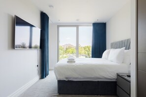 Habitació d'hotel moderna amb un llit gran, una televisió de pantalla plana penjada a la paret i vista a la ciutat per la finestra.