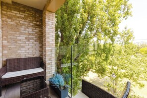A balcony with wicker furniture, a potted plant, and a view of trees. - Modern Parkside Flat with Balcony in Kilburn (Greater London)