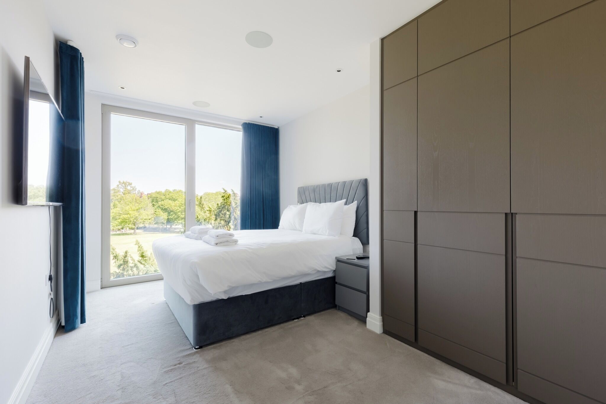 A modern bedroom with a large bed, a nightstand, and a wardrobe.