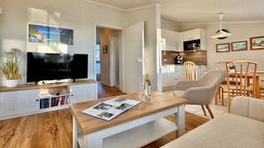 Un salon moderne doté d’un téléviseur à écran plat, d’une table basse en bois et d’un coin repas avec des chaises et une table.