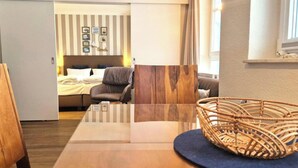 Hotellihuone, jossa on sänky, tuoli, pöytä ja punottu kori.