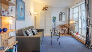 A living room with a sofa, a table, a bookshelf, a window with curtains, and a door with shutters. - Moderne Ferienwohnung im Seepark Sellin (Sellin)