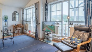 A living room with a television, a chair, a table, and large windows. - Moderne Ferienwohnung im Seepark Sellin (Sellin)