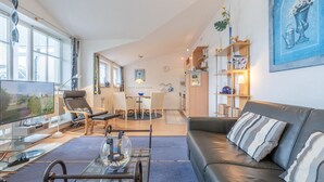 A modern living room with a sofa, TV, and a dining area with chairs and a table. - Moderne Ferienwohnung im Seepark Sellin (Sellin)