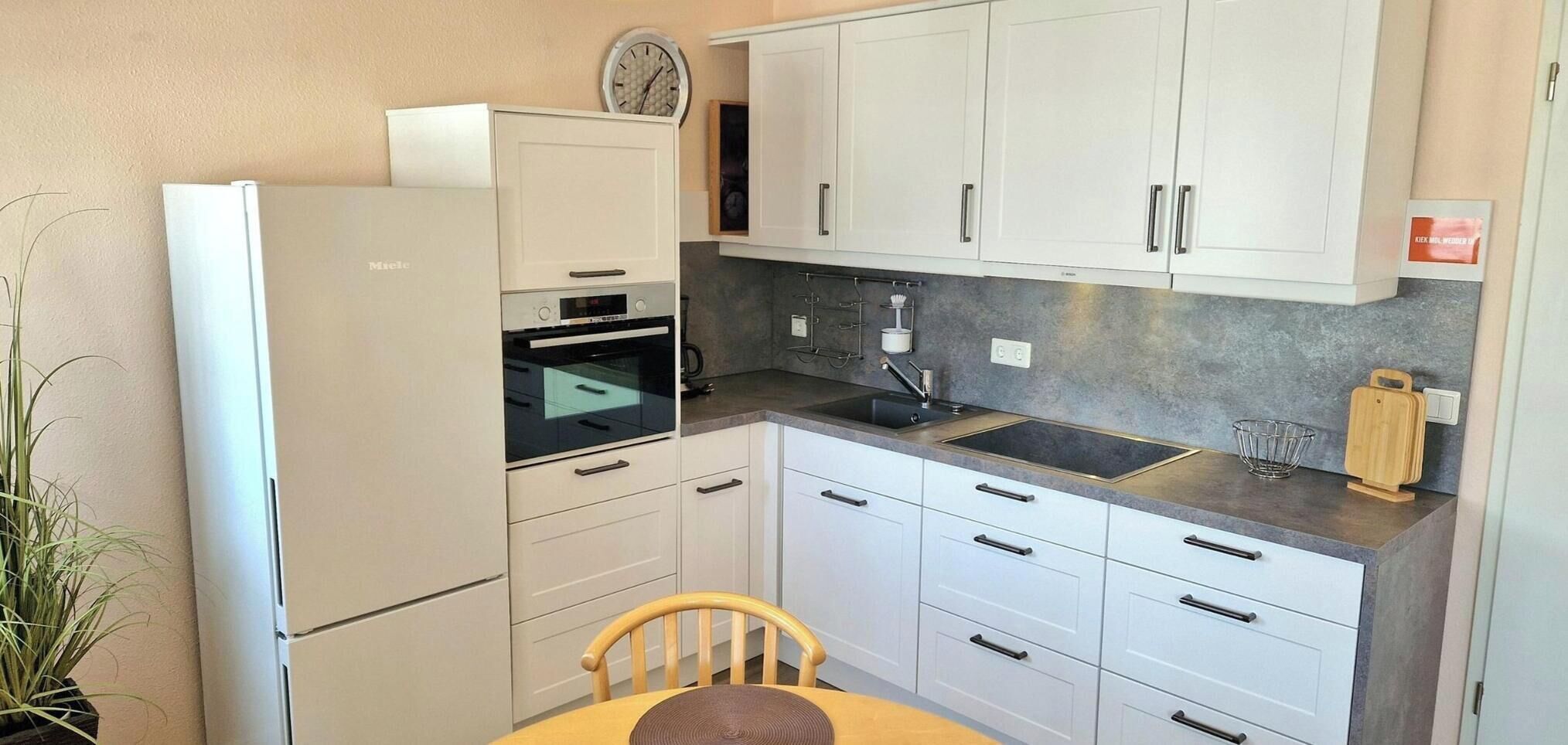 A compact kitchen with white cabinets, a built-in oven, a sink, and a clock on the wall.