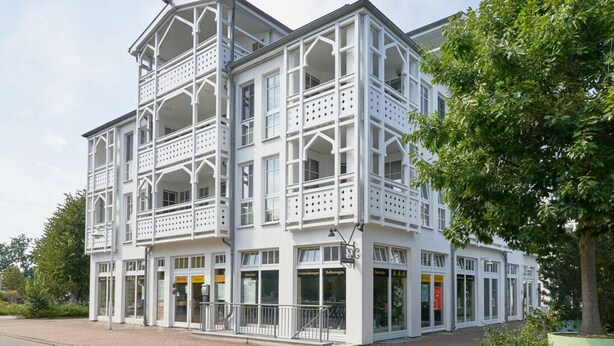 A white building with multiple balconies and storefronts, featuring a traditional architectural style. - Ferienwohnung im 3.OG mit Balkon in Sellin (Sellin)