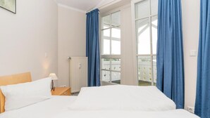A hotel room with a bed, a nightstand, a lamp, a window with curtains, and a view of a balcony. - Ferienwohnung im 3.OG mit Balkon in Sellin (Sellin)