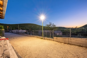 A fenced outdoor area with a sandy ground, a concrete wall, and a streetlight. - Pool Villa Marija (Unesic)