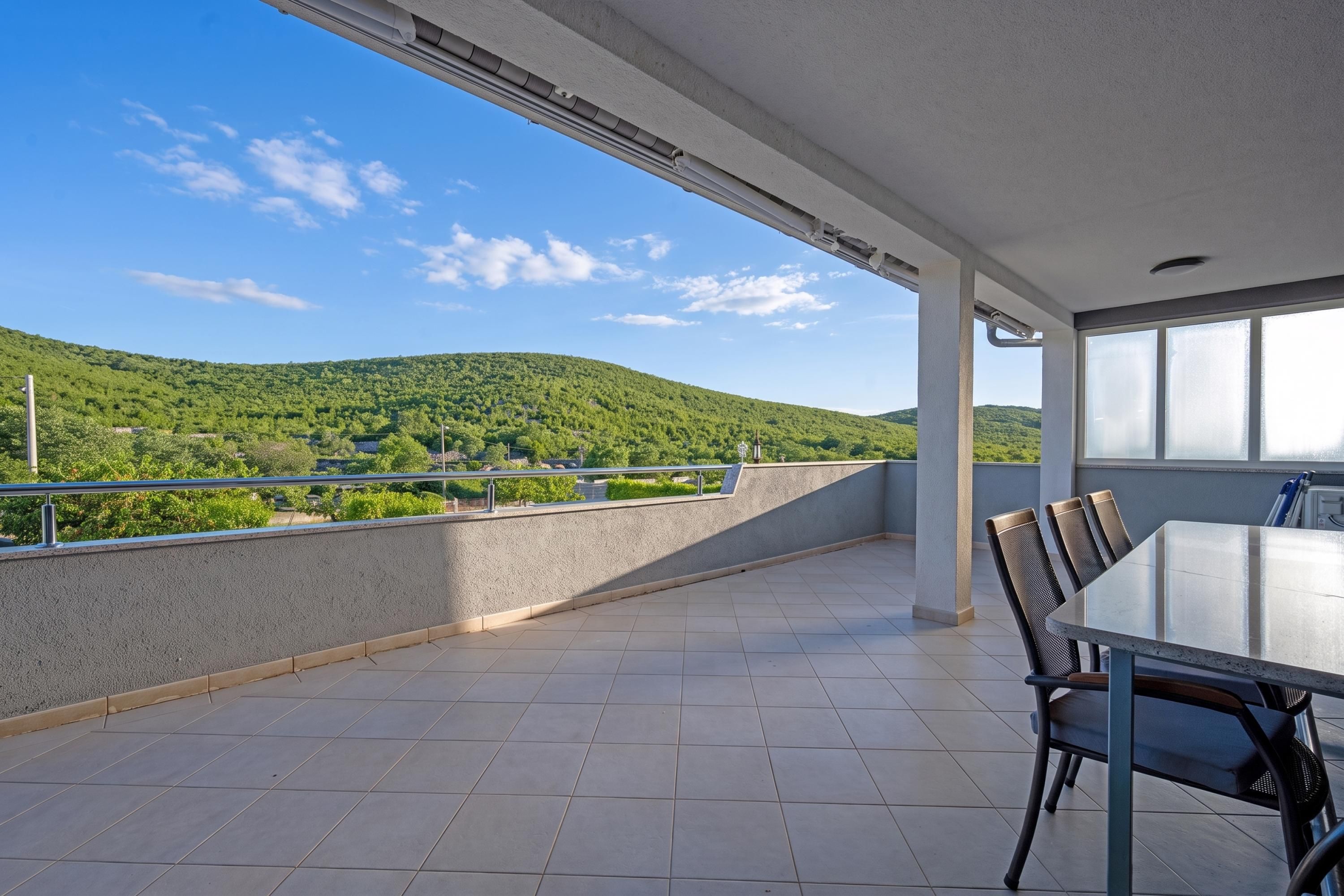 Een balkon met uitzicht op groene heuvels, een tafel met stoelen en een hekwerk.