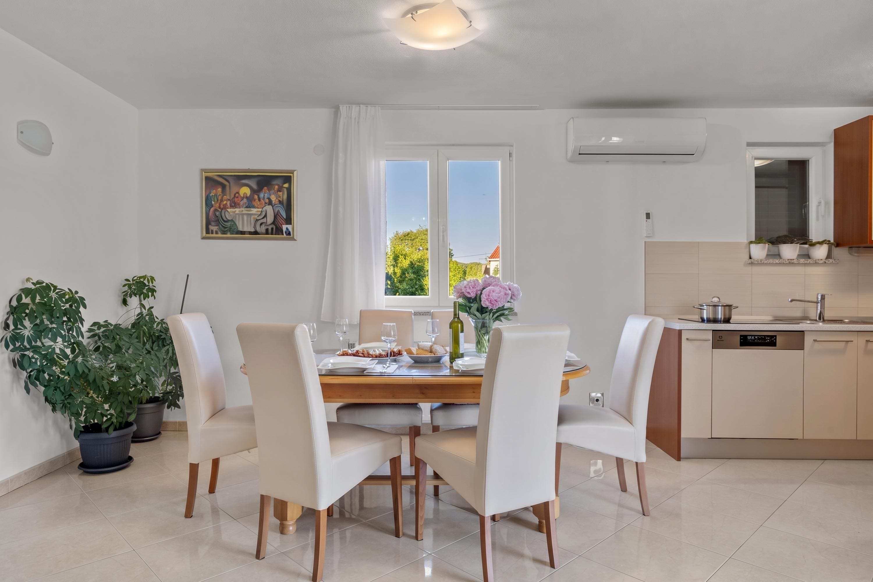 A dining area with a table set for four, surrounded by chairs, a window with curtains, and a painting on the wall.