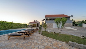 A poolside area with lounge chairs, a stone patio, and a building with a satellite dish. - Pool Villa Marija (Unesic)