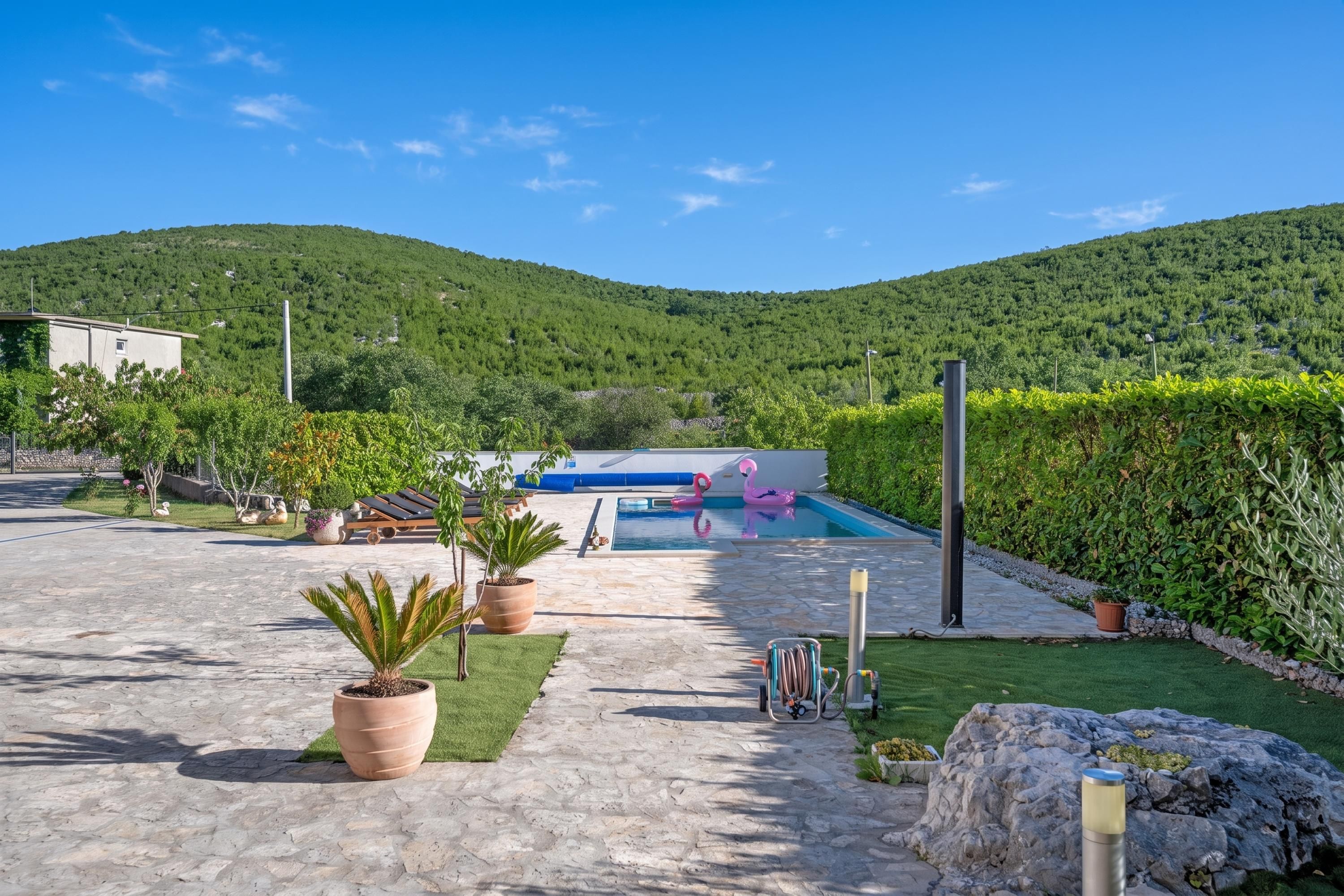 A pool area with lounge chairs, a small pool, and a view of a green hillside.