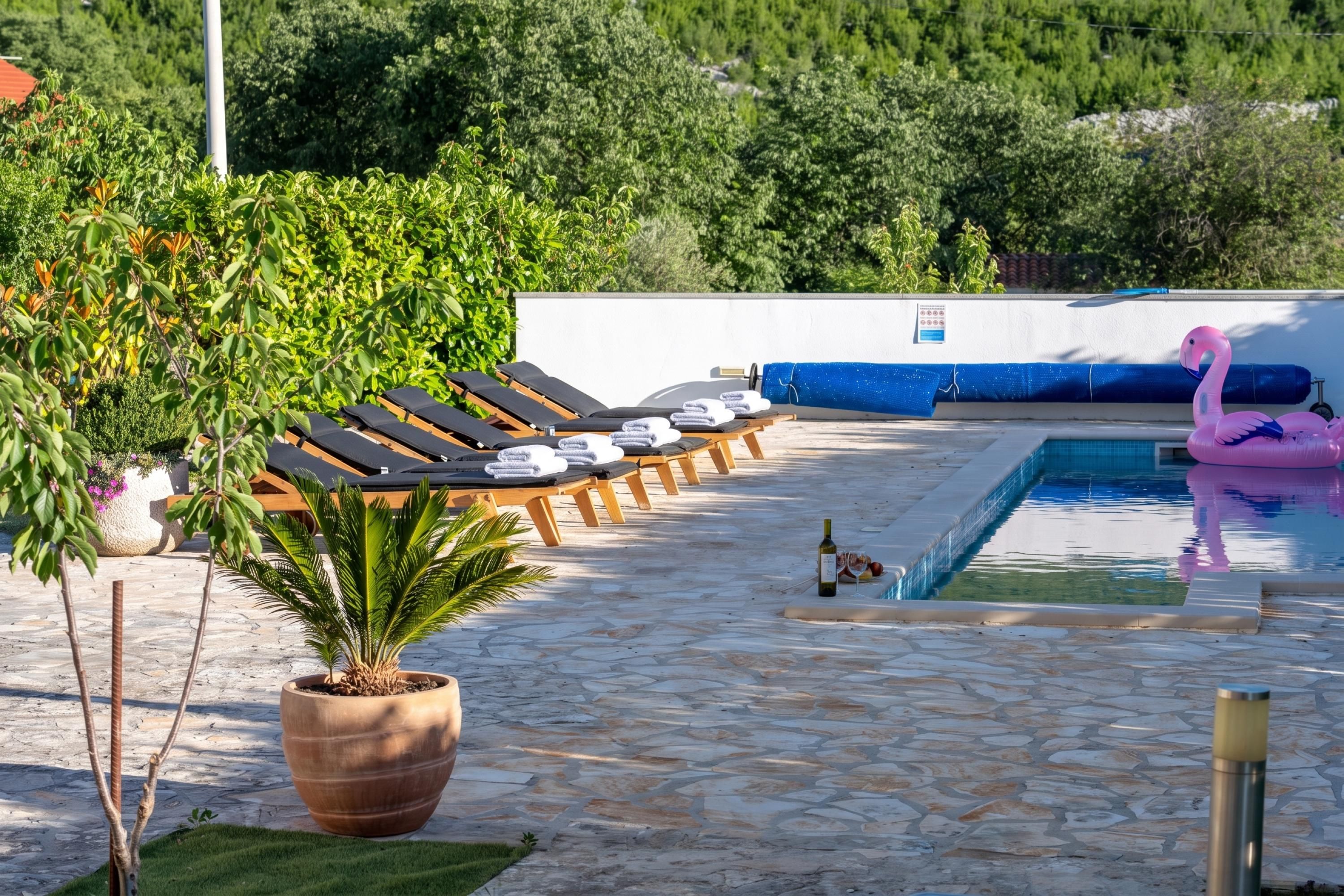A poolside area with lounge chairs, a potted plant, and a flamingo float.