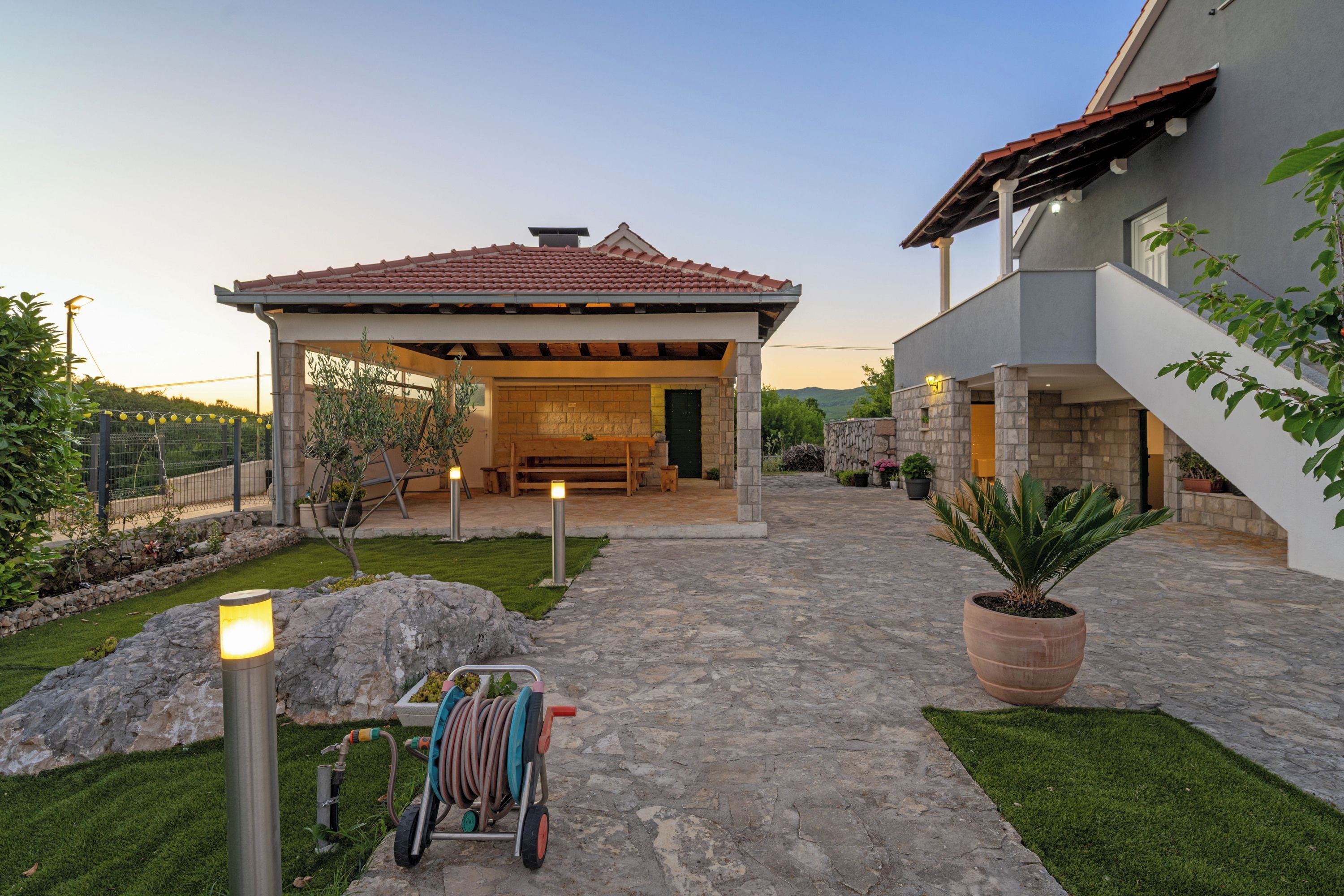 A modern house with a stone patio, a covered outdoor seating area, and a large potted plant.