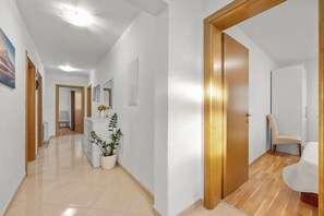 Un pasillo con una puerta de madera, un aparador blanco y una planta en maceta.