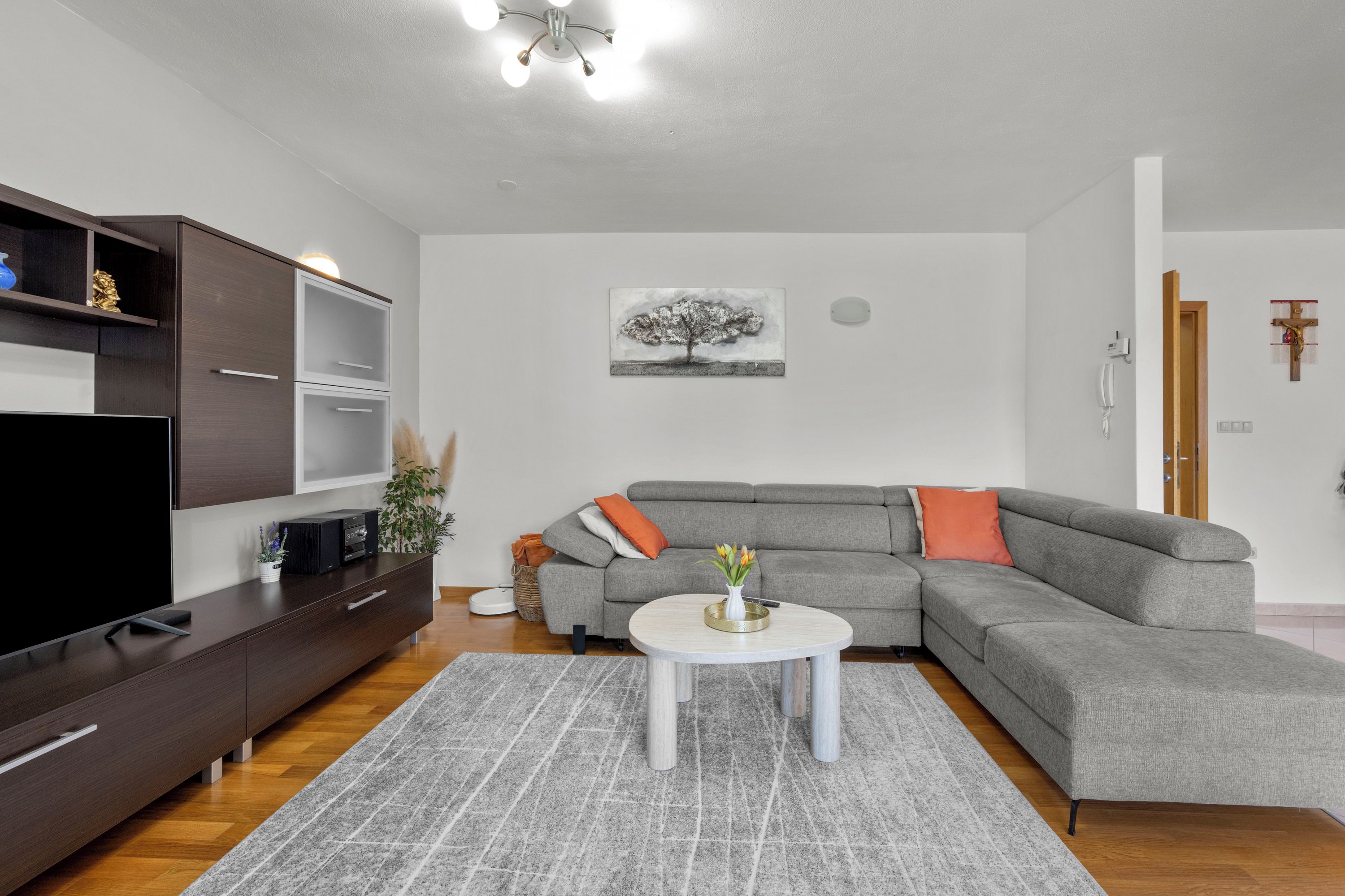 A modern living room with a sectional sofa, a flat-screen TV, a coffee table, and a painting on the wall.