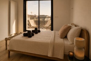 Une chambre à coucher avec un lit, des oreillers, une table de chevet avec une bougie et une vue sur l’extérieur.