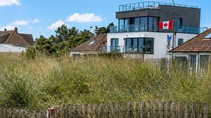 Een modern gebouw met een Canadese vlag, omringd door hoog gras en een houten hek.