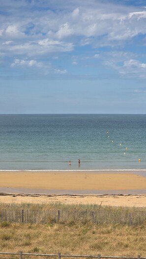 Une plage avec une clôture au premier plan, un ciel dégagé et une mer calme.