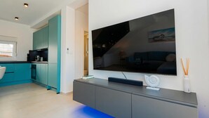 A modern kitchen with teal cabinets, a large flat-screen TV, and a grey entertainment unit. - Pool Villa Pomalo (Vodice)
