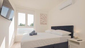 A bedroom with a bed, a nightstand, a TV mounted on the wall, and a window. - Pool Villa Pomalo (Vodice)