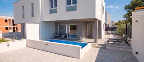 A modern two-story house with a swimming pool, outdoor seating, and a clear sky.