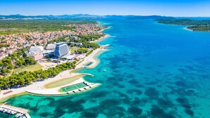 An aerial view of a coastal town with a marina, clear blue waters, and a mix of residential and commercial buildings. - Pool Villa Pomalo (Vodice)