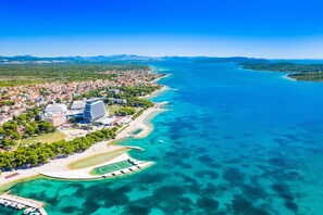 Vista aérea de un pueblo costero con un puerto deportivo, aguas azul cristalino y una combinación de edificios residenciales y comerciales.