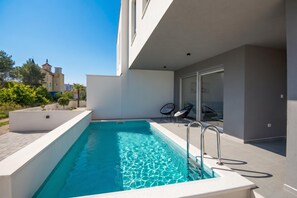 Un edificio moderno con piscina, asientos exteriores y vistas a edificios cercanos.