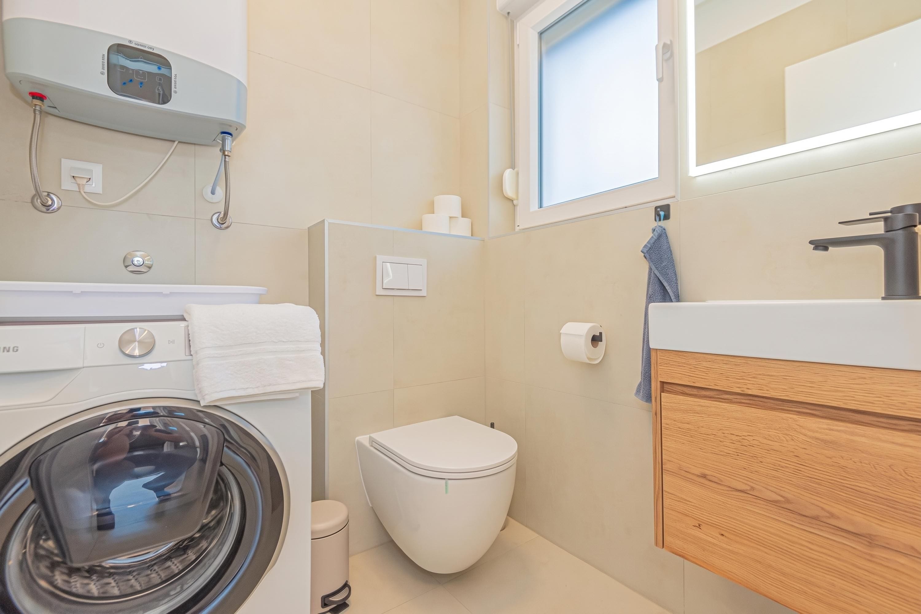 Un baño pequeño con lavadora, inodoro y un armario de madera.