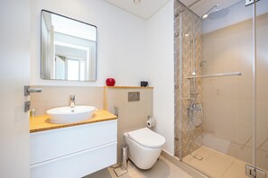 Uma casa de banho moderna com lavatório, sanita, chuveiro e espelho.