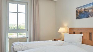 Hotellihuone, jossa on suuri ikkuna, sänky, yöpöytä lampun kanssa ja taulu seinällä.